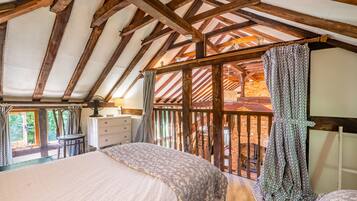 A bedroom with a wooden ceiling, a bed, a dresser, and a window with curtains.