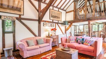 A spacious room with exposed wooden beams, a pink checkered sofa, a pink sofa, and a wooden coffee table.