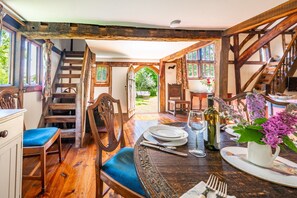 A wooden dining area with a table set for two, a staircase, and a view of the outdoors. - Tudor style timber framed forest lodge - The Pink House (Bury St Edmunds)