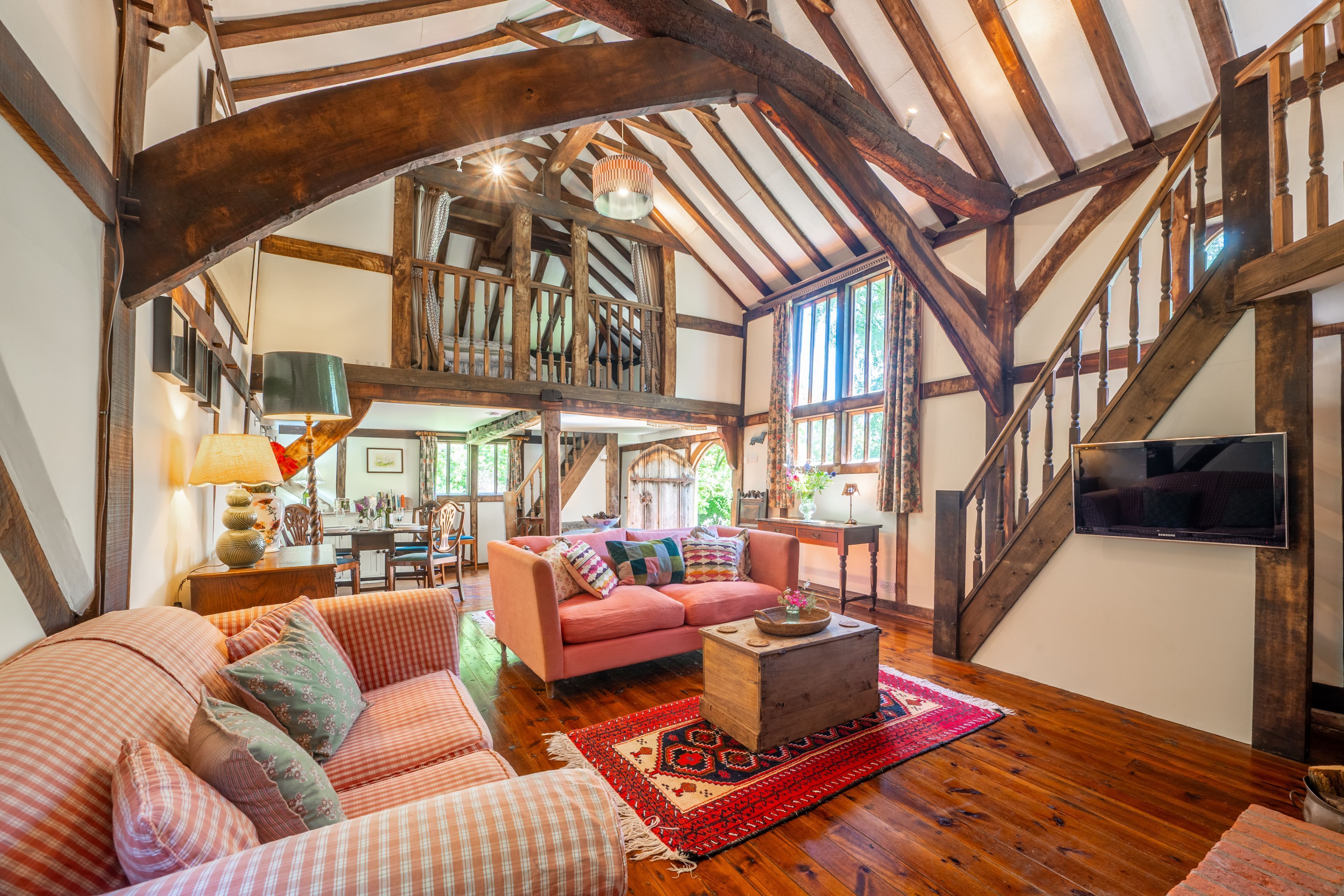 A spacious living room with a high ceiling, wooden beams, a pink sofa, a coffee table, and a television.