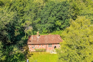 A traditional red-roofed house surrounded by dense green foliage. - Tudor style timber framed forest lodge - The Pink House (Bury St Edmunds)