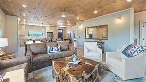 Un espacio habitable amplio con techo de madera, un sofá con un cojín que dice 'USA', una mesa de centro y un sillón blanco.