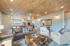 Ein geräumiger Wohnbereich mit Holzboden, einem Sofa mit einem 'USA'-Kissen, einem Couchtisch und einem weißen Sessel.