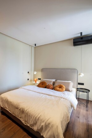 A modern bedroom with a large bed, a bedside table, a lamp, and a wall-mounted air conditioner.