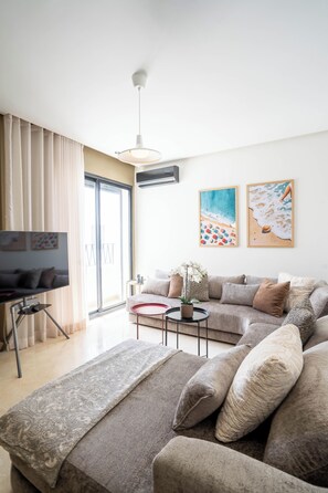 A modern living room with a sofa set, a television, and a large window with curtains.