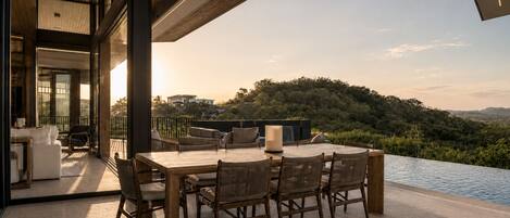 A dining area with a table and chairs, overlooking a pool and a scenic landscape.