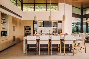 A modern kitchen with a central island, wooden cabinetry, and pendant lighting. - New · 180° Views – River & National Park · Infinity Pool · 3 min to the Beach (Tamarindo)
