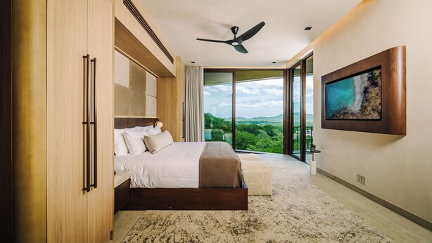 Ein modernes Schlafzimmer mit einem großen Bett, einem Deckenventilator und Blick ins Freie.