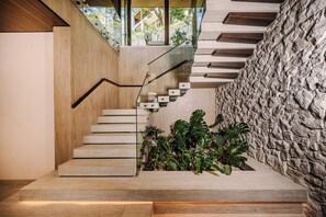 A modern staircase with a wooden finish, a stone wall, and a view of greenery outside. - New · 180° Views – River & National Park · Infinity Pool · 3 min to the Beach (Tamarindo)
