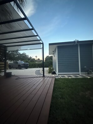 Un espace extérieur abrité doté d’une terrasse en bois, d’un garage et d’un véhicule garé au fond.