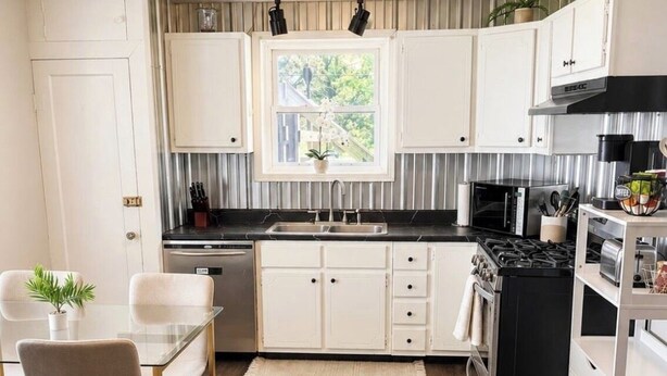 A modern kitchen with white cabinets, a black stove, and a dining area with a glass table and chairs. - The Red Door, a cozy and stylish retreat in the heart of Newton, Illinois. (Newton)