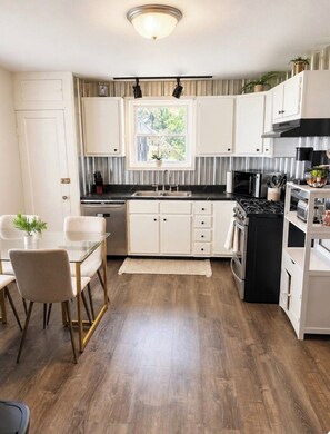 A modern kitchen with white cabinets, a black stove, and a dining area with a glass table and chairs.
