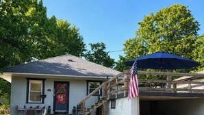 A single-story house with a front porch, a staircase leading to a garage, and an American flag. - The Red Door, a cozy and stylish retreat in the heart of Newton, Illinois. (Newton)