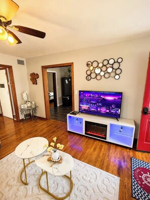 A living room with a flat-screen TV, a fireplace, a ceiling fan, and a decorative wall piece.
