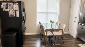 A kitchen with a dining table, chairs, a refrigerator, and a trash bin. - The Red Door, a cozy and stylish retreat in the heart of Newton, Illinois. (Newton)