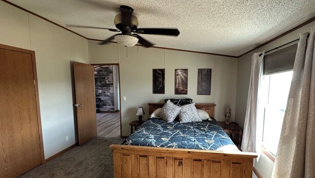 A bedroom with a wooden bed, a ceiling fan, a door, and a window with curtains.