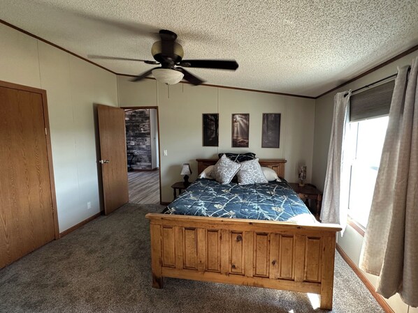A bedroom with a wooden bed, a ceiling fan, a door, and a window with curtains.
