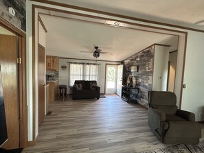 A spacious living area with a ceiling fan, a sofa, a chair, and a kitchen in the background.
