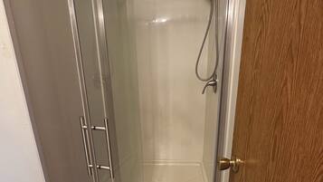 A glass-enclosed shower with a showerhead and a drain, a wooden door, and a tiled floor.