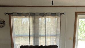 A room with a sofa, a mattress, a clock, and a window with curtains.