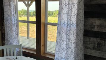 A room with a wooden interior, a window with a view of a field, and a table with a chair.