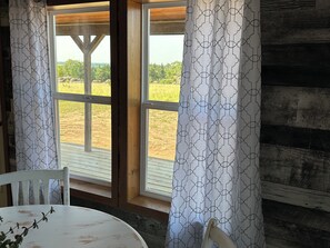 A room with a wooden interior, a window with a view of a field, and a table with a chair.