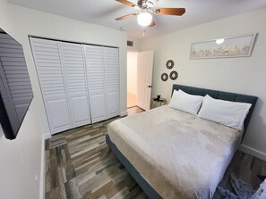 Ein Schlafzimmer mit einem Bett, einem Deckenventilator, einem Kleiderschrank und einer Tür zu einem anderen Raum.