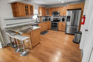 A modern kitchen with wooden cabinets, stainless steel appliances, a granite countertop, and a bar stool area. - Beautiful 4-bedroom House With Heated Swimming Pool & Spa (Fort Lauderdale)