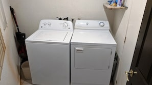 A laundry room with two white front-loading washing machines and a shelf with cleaning supplies. - Sonoran Spa Ground Floor 109-W (Puerto Peñasco)