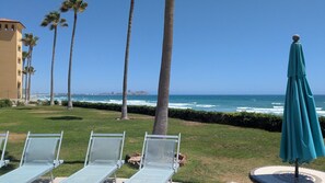 Eine Strandlounge mit Stühlen und Sonnenschirm, Palmen und Blick auf das Meer.