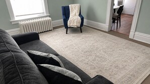 Un salon avec un canapé gris foncé, un fauteuil bleu agrémenté d’un plaid blanc et un tapis à motifs.