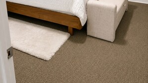 A bedroom with a bed, a bench, and a carpeted floor.
