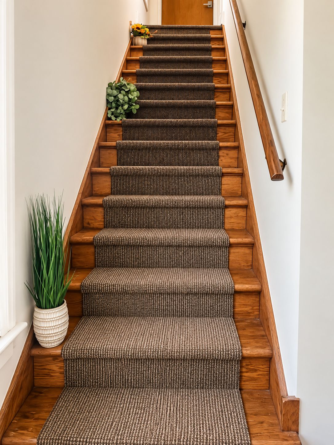 A wooden staircase with a textured carpet runner and a potted plant beside it.