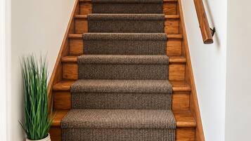A wooden staircase with a textured carpet runner and a potted plant beside it.