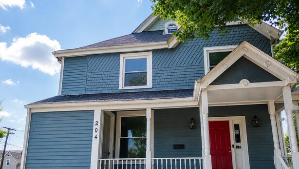 A two-story house with a red door and a white porch railing.