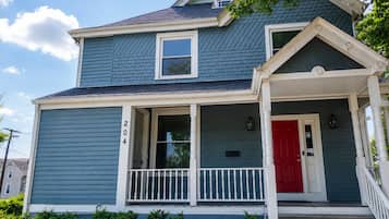 A two-story house with a red door and a white porch railing.