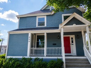 A two-story house with a red door and a white porch railing.