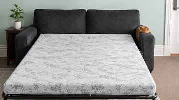 A bed with a floral mattress, a dark sofa, a small table with a plant, and a door in the background.