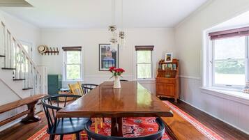 A dining room with a wooden table, chairs, a vase with flowers, a bookshelf, and a staircase.