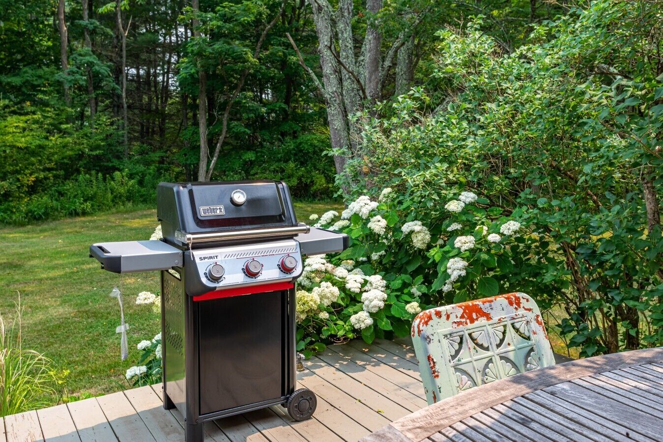 A Weber Spirit grill on a wooden deck with a garden backdrop.
