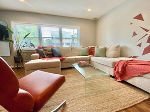 A living room with a sofa, a glass coffee table, and a red chair. - Direct PATH & Bus to NYC | MetLife 20 min | Parking + Deck (Jersey City)