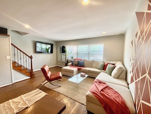 Ein Wohnzimmer mit Sofa, Sessel, Couchtisch und einem an der Wand montierten Fernseher.
