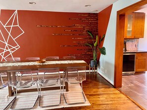 A dining area with a wooden table, clear glass chairs, and a geometric wall decoration. - Direct PATH & Bus to NYC | MetLife 20 min | Parking + Deck (Jersey City)