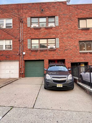 Un immeuble de deux étages en briques, avec un garage, une voiture garée devant et une porte verte.