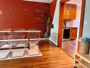 Un coin repas avec une table et des chaises en bois, un mur d’accent rouge et une cuisine visible à travers une porte ouverte.