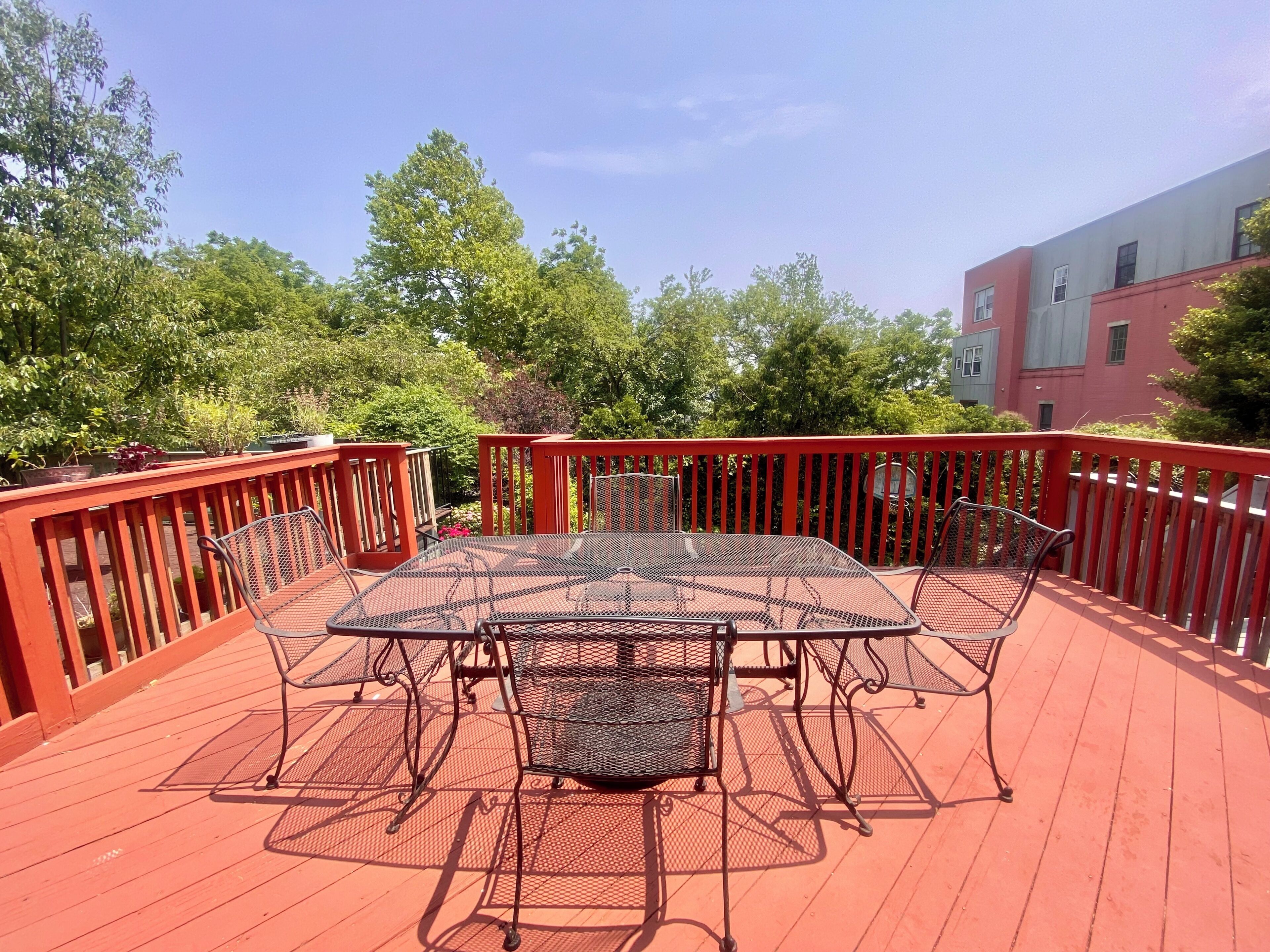 A covered outdoor deck with a metal table and chairs, surrounded by a red railing.