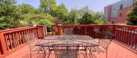 A covered outdoor deck with a metal table and chairs, surrounded by a red railing.