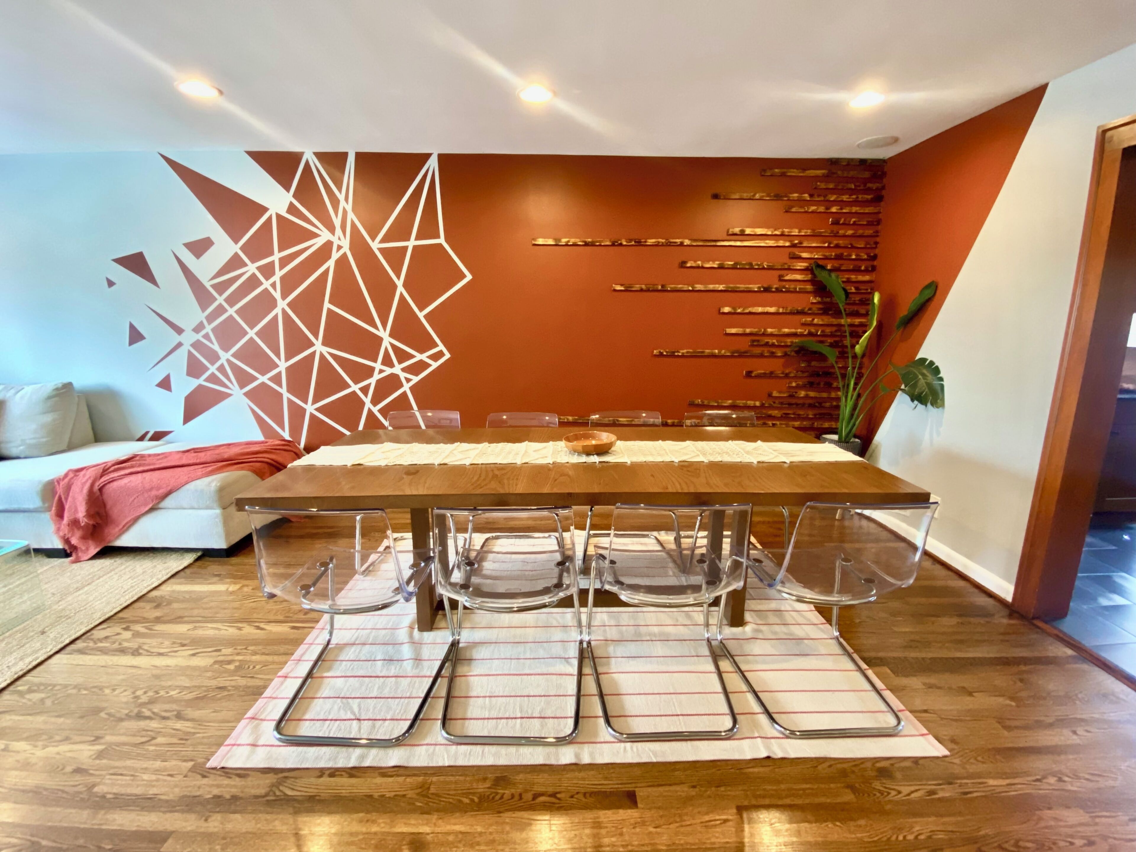 Een eetruimte met een lange tafel, transparante stoelen en een decoratieve wand met geometrische patronen.