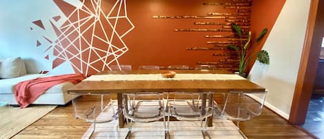 Een eetruimte met een lange tafel, transparante stoelen en een decoratieve wand met geometrische patronen.