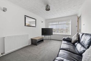 Een moderne woonkamer met een leren bank, een flatscreen televisie, een klein houten tafeltje en een radiator.